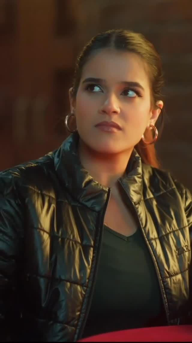 Close-up of a woman in a glossy black puffer jacket and hoop earrings, lit in warm tones